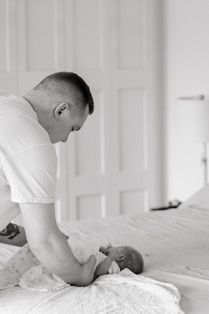 Parents admiring their newborn baby during a cozy in-home newborn photography session with a Michigan newborn photographer.