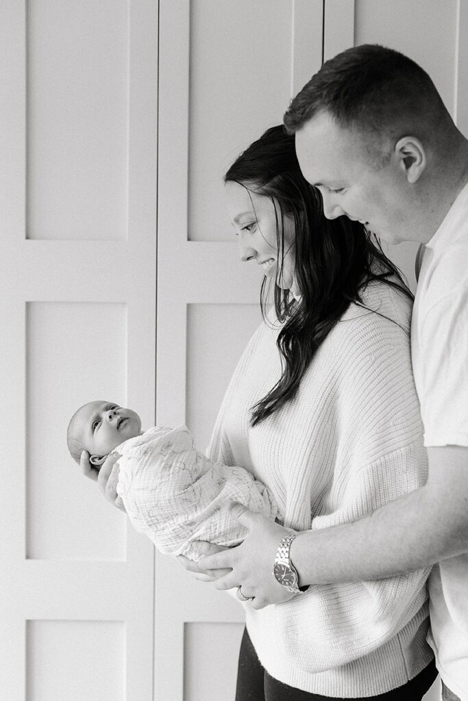 Parents admiring their newborn baby during a cozy in-home newborn photography session with a Michigan newborn photographer.