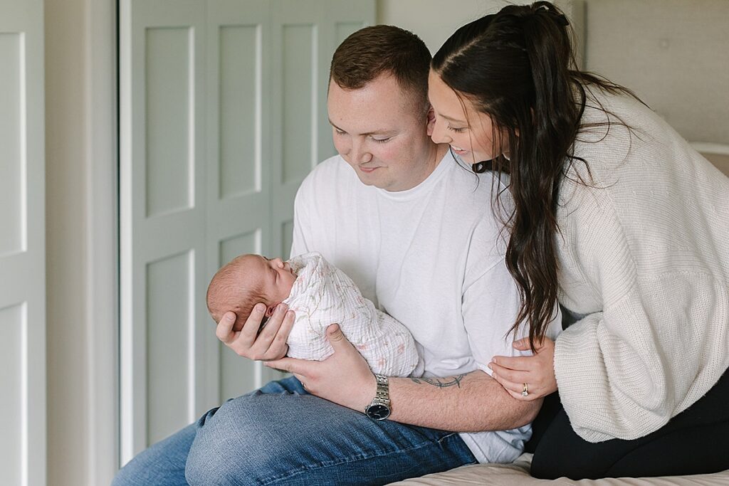 Parents admiring their newborn baby during a cozy in-home newborn photography session with a Michigan newborn photographer.