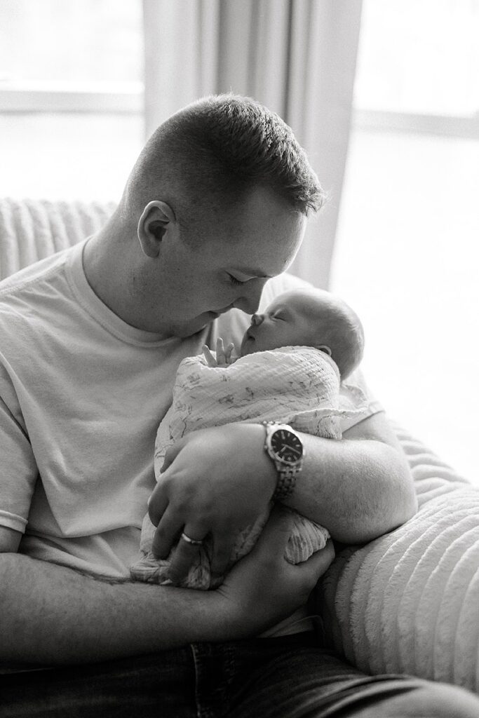 Father gently holding his newborn baby in the nursery during a relaxed in-home newborn photography session.