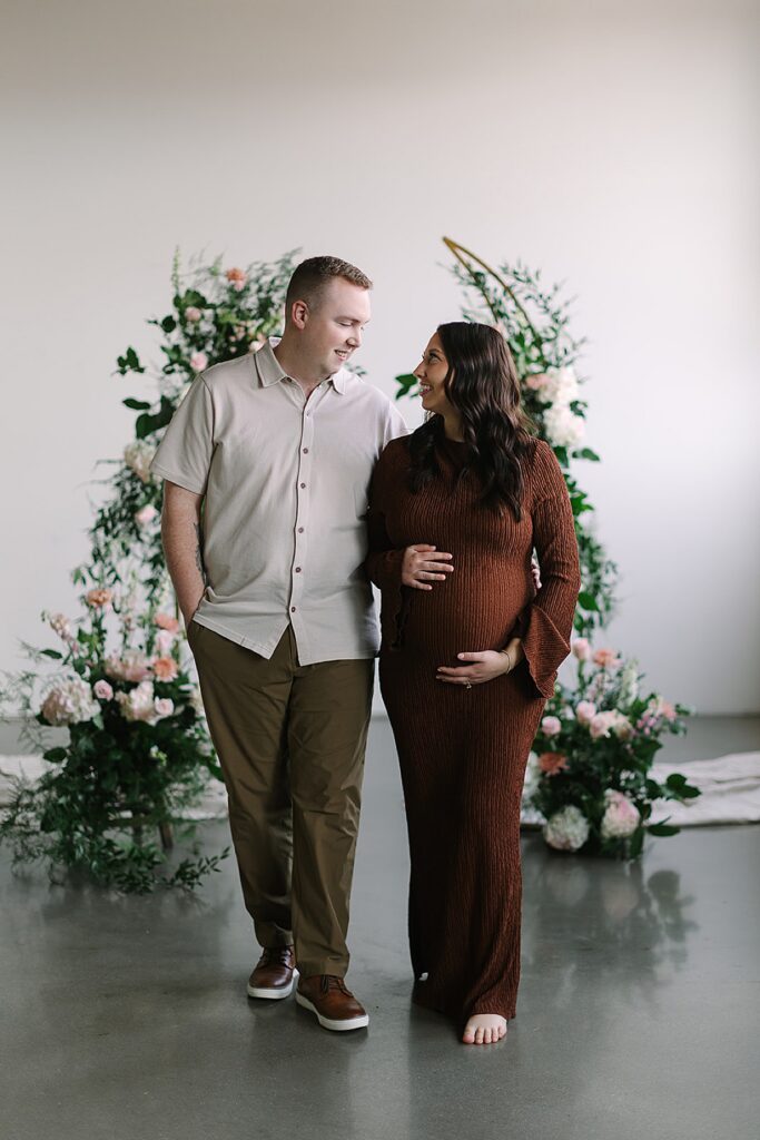 Couple posing in a floral installation during a winter maternity photography session with a Michigan maternity photographer.