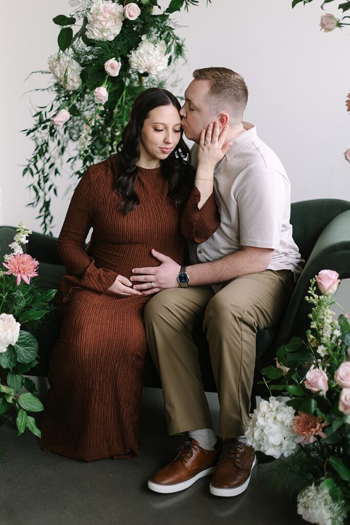 Couple posing in a floral installation during a winter maternity photography session with a Michigan maternity photographer.