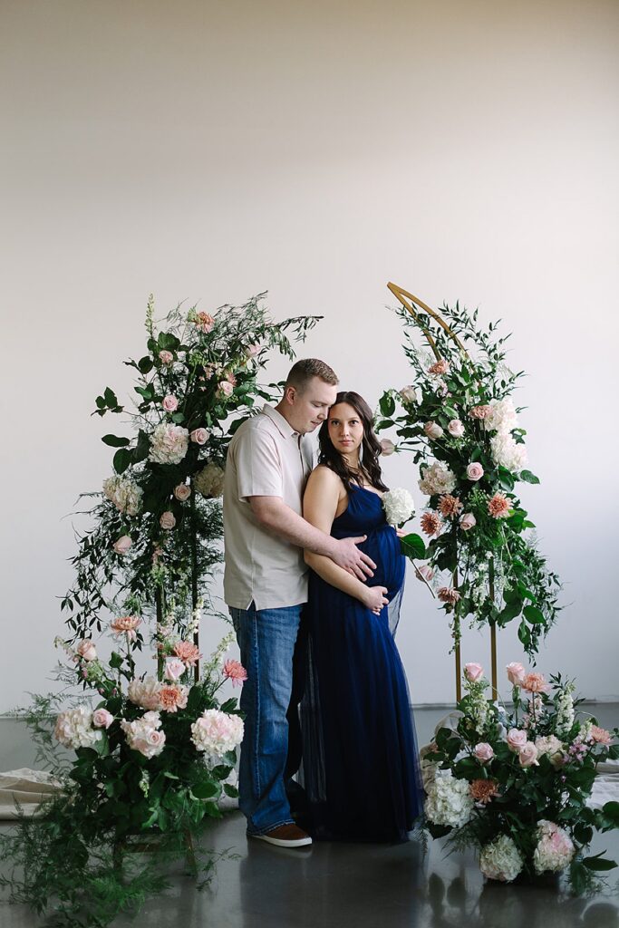 Couple posing in a floral installation during a winter maternity photography session with a Michigan maternity photographer.